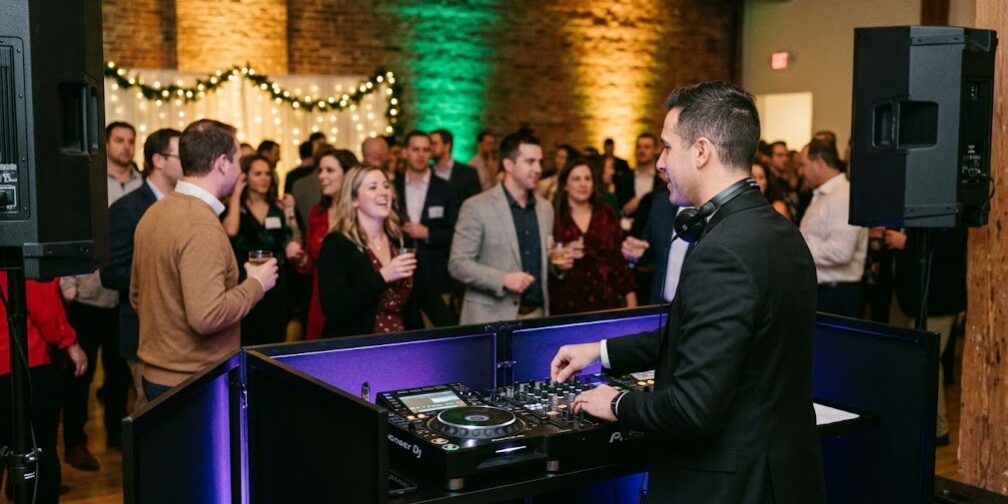 A professional DJ with modern equipment and dynamic uplighting entertains a lively corporate holiday party crowd in Rochester NY.