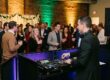 A professional DJ with modern equipment and dynamic uplighting entertains a lively corporate holiday party crowd in Rochester NY.