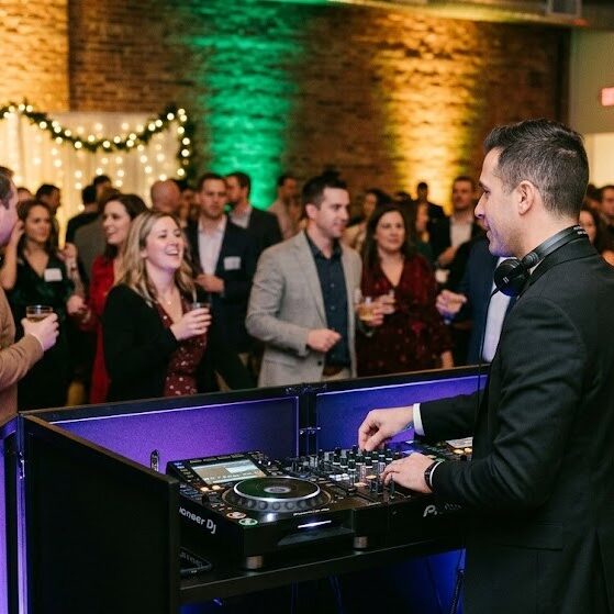 Professional Rochester NY Holiday Party DJ and Event Lighting A professional DJ with modern equipment and dynamic uplighting entertains a lively corporate holiday party crowd in Rochester NY.
