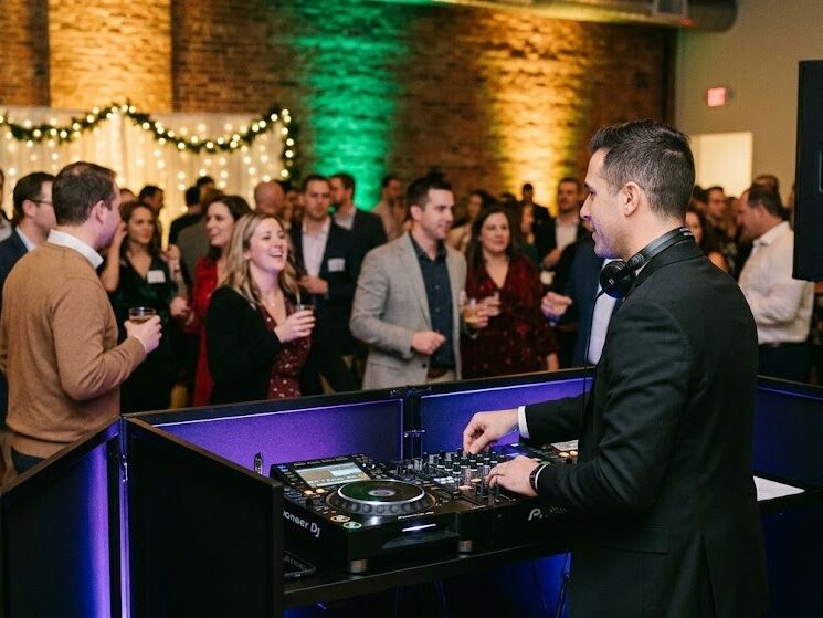 Professional Rochester NY Holiday Party DJ and Event Lighting A professional DJ with modern equipment and dynamic uplighting entertains a lively corporate holiday party crowd in Rochester NY.
