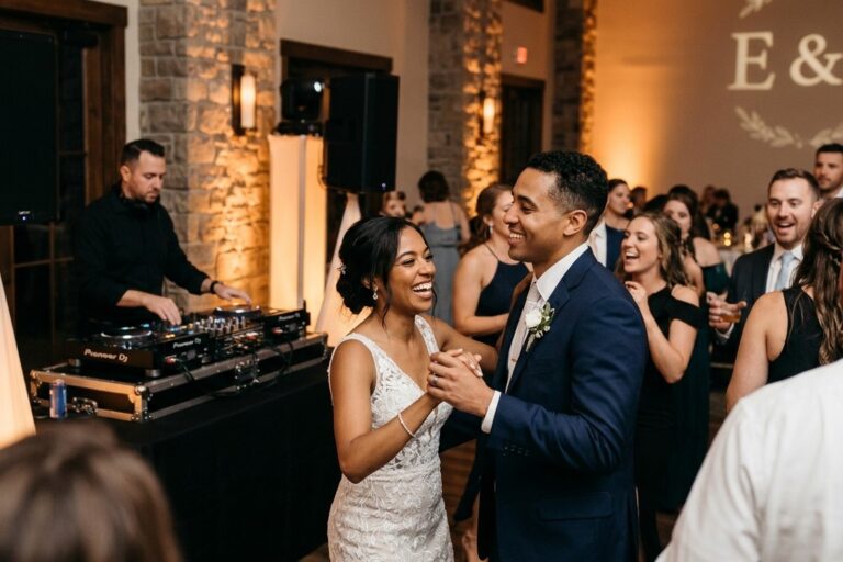 A smiling bride and groom dancing on a packed dance floor during a wedding reception with a professional wedding DJ and custom monogram lighting in Rochester NY.